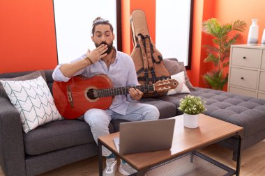 Sakallı İspanyol bir adam evde klasik gitar çalıyor ağzını eliyle kapatıyor, şok geçiriyor ve hata yapmaktan korkuyor. şaşırmış ifade 