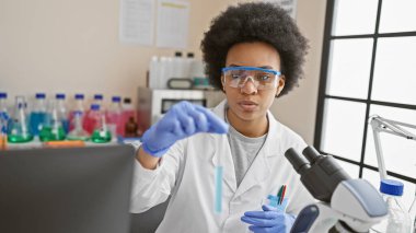 Modern bir laboratuvar ortamında test tüpü içeriğini analiz eden odaklanmış Afrikalı Amerikalı kadın bilim adamı..