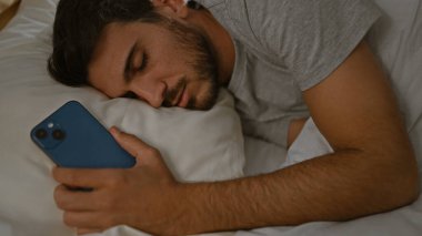 Genç bir İspanyol, elinde akıllı telefon tutarken yatak odasında huzur içinde uyuyor..
