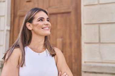 Kollarını kavuşturmuş genç, güzel İspanyol kadın caddede gökyüzüne bakıyor.