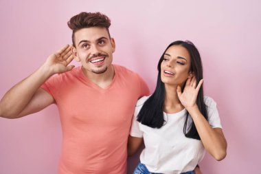 Pembe arka planda dikilen genç İspanyol çift el pençe divan durup dedikoduları dinliyor. Sağırlık kavramı. 