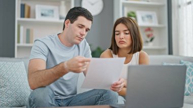 Evdeki kanepede oturmuş dizüstü bilgisayar okuyan güzel bir çift.