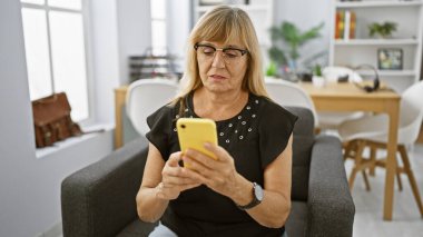 Başarılı bir iş, orta yaşlı sarışın kadın işçi akıllı telefonuna bir mesaj yazıyor, ek iş olarak ofis koltuğundan çalışıyor.