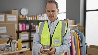 Yansıtıcı yelek giymiş, özverili bir şekilde gönüllü olarak hayır kurumunda çalışan, akıllı telefonuna bir sürü bağış kutusunun arasında özenle mesaj yazan orta yaşlı bir adam..