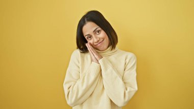 Genç İspanyol bir kadın, canlı sarı bir arka plana karşı nazik bir gülümsemeyle poz verir, sıcaklık ve pozitiflik yayar..
