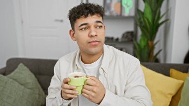 Yakışıklı genç adam rahat, modern bir oturma odasında kahvesini içiyor.