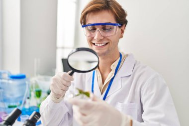 Young caucasian man scientist looking plant sample with loupe at laboratory