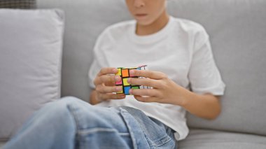 Kanepede oturan sarışın çocuk evde rubik küple oynuyor.