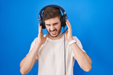 Sakallı, müzik dinleyen, kulaklık takan, parmaklarıyla kulaklarını kapatan, gürültülü müzik sesi için rahatsız edici ifadeler takan İspanyol bir adam. sağır kavramı. 