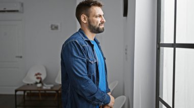 Yakışıklı, genç İspanyol bir adam, düşüncelere dalmış, bekleme odasının penceresinden bakıyor, havalı ama ciddi bir ifadeyi canlandırıyor. Sıradan yaşam tarzını sergileyen kapalı mekan portresi.