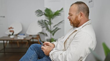 Yakışıklı, orta yaşlı, sakallı beyaz adam. Bekleme odasında akıllı telefonuyla neşeli bir selfie çekerek eğleniyor. Gülüşü ışıl ışıl..