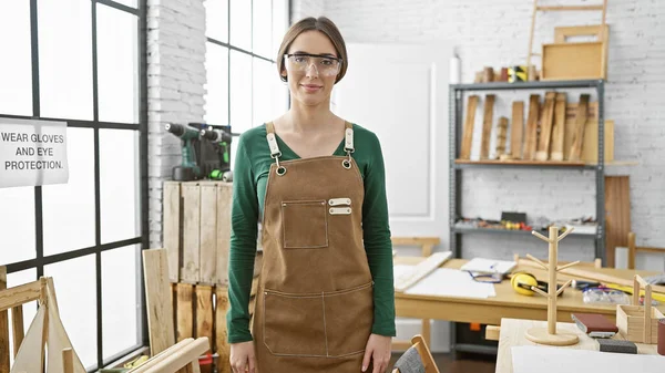 自信的女木匠戴着安全眼镜站在设备齐全的木工车间里 — 图库照片