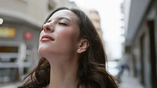 stock image A young hispanic woman with a serene expression stands outdoors on a city street, embodying urban beauty and style.