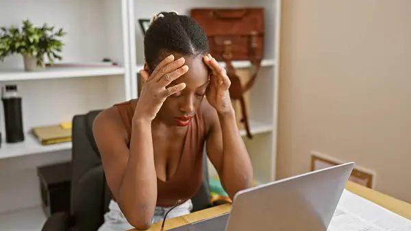 Stressed african american business woman working hard on laptop at office, overworked and worried amid professional challenges
