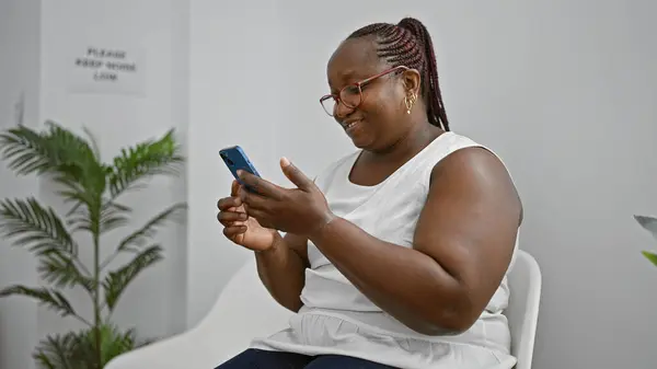自信的非洲裔美国女性老板 头戴辫子 坐在候车室里 愉快地用智能手机发短信 — 图库照片