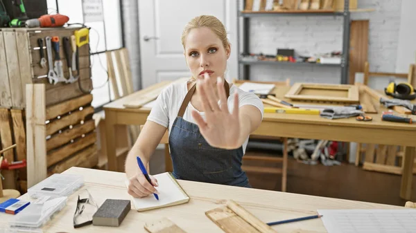 一个穿着粗斜纹棉布围裙的年轻女子打算在木工工作室里做木工活时停下来 — 图库照片