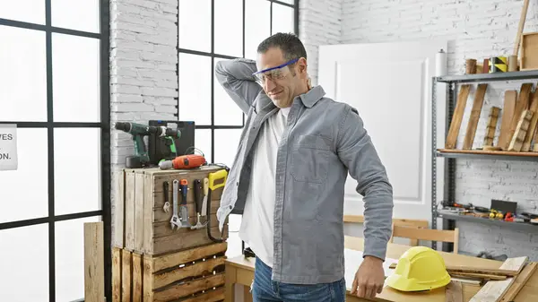在一个精心组织的木工车间里 一个用各种工具和安全帽表达背痛的恐慌男人 — 图库照片