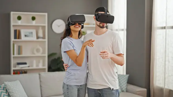 Gorgeous couple sharing love, gaming together with vr glasses at home, exploring futuristic cyber world, smiling and hugging in their cozy living room.