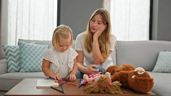 Stressed mother relaxing on sofa at home while little caucasian daughter seriously engages in drawing on notebook indoors