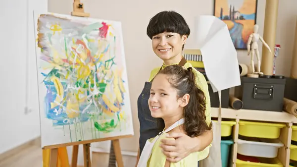 In the heart of the art studio, a confident teacher artist and a smiling student sharing a warm hug, standing next to their vibrant canvas draw.