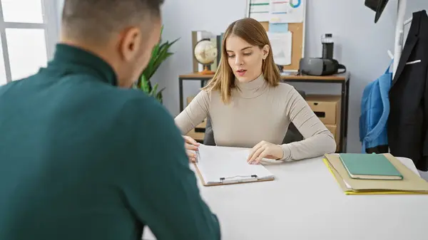 stock image Man and woman discuss documents in a modern office setting, depicting teamwork and professional collaboration.