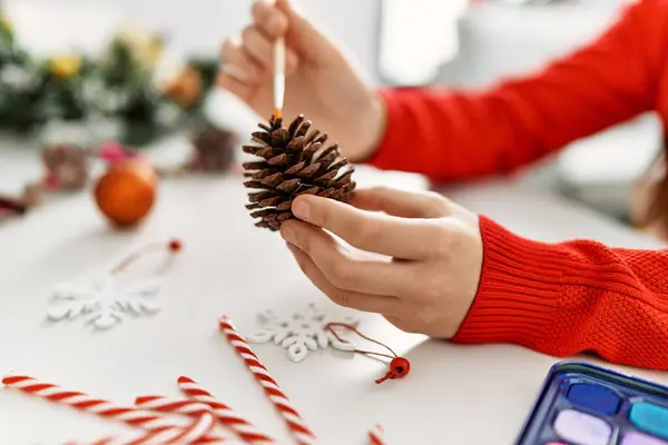 Young caucasian woman painting christmas decoration sitting on table at home