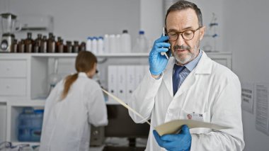 Bilimin kalbinde, iki sadık laboratuvar arkadaşı, erkek ve kadın bilim adamı, akıllı telefonla konuşuyorlar, laboratuvar analizleri ve araştırmalar sırasında birlikte belge okuyorlar.