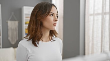 Düşünceli bir ifadeyle genç bir İspanyol kadın. Parlak, modern bir yatak odasında. Güzellik ve sükunet duygusu taşıyor..