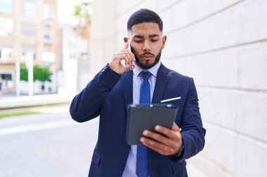 Sokakta akıllı telefondan konuşan genç Latin iş adamı touchpad kullanıyor.