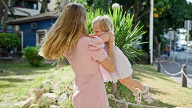 Parkta dans eden neşeli anne, kollarında gülümseyen kızı, güneşi ıslatan, neşe içinde güneşlenen