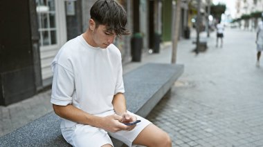 Havalı, genç İspanyol bir adam, telefonuna dalmış, günümüzün teknoloji meraklısı gençlik yaşam tarzının sıradan bir portresini çiziyor.