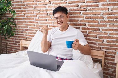 Genç Asyalı adam kahve içiyor yatakta oturmuş gururla bağırıyor, zaferi kutluyor ve kollarını kaldırarak çok heyecanlanıyor. 