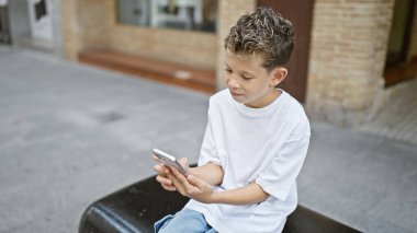 Sevimli sarışın çocuk mesajlaşmayı çok seviyor. Telefon teknolojisini kullanıyor. Şehir bankında rahatça oturuyor.