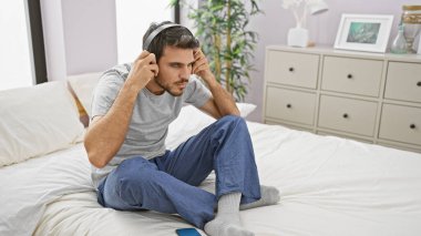 Yatak odasında sakallı İspanyol bir adam oturmuş, kulaklıkla müzik dinliyor, düşünceli bakışlar atıyor..