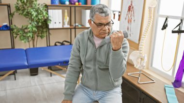 Olgun bir erkek, rehabilitasyon kliniğinin terapi odasında dambılla egzersiz yapar. Sağlık ve kıdemli sağlık hizmetleri sunar..