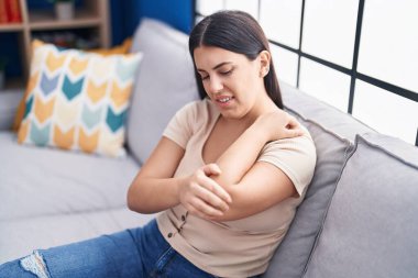 Kanepede oturan genç, güzel İspanyol kadın evde dirsek ağrısı çekiyor.