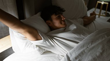 Mutlu İspanyol genç kollarını sabah yatağında esnetiyor, kendine güvenerek aydınlık bir yatak odasında uyanıyor.