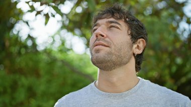 Genç adam parkta ciddi bir ifadeyle yan tarafa bakıyor.