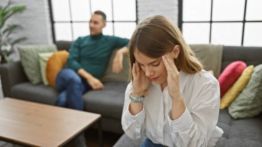 Başı ağrıyan sıkıntılı bir kadın ve rahat bir oturma odasında ilişki sorunları tasvir eden endişeli bir adam..