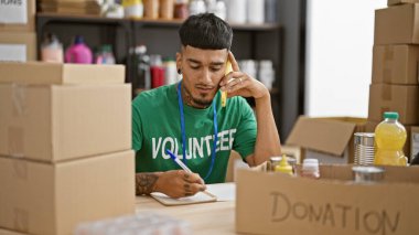 Çalışkan Latin bir adam hayır kurumunda gönüllü olarak çalışıyor, akıllı telefondan konuşuyor ve notlar alıyor, dövmelerini sergiliyor.