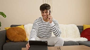 Genç İspanyol adam evde dokunmatik ped kullanarak akıllı telefondan konuşuyor.