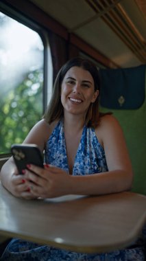 Gülümseyen güzel İspanyol kadın, modern metro yolculuğu sırasında mutlu bir şekilde telefonuna mesaj atıyor.