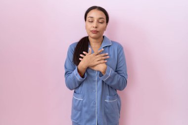 Mavi pijama giyen, elleri göğsünde, gözleri kapalı gülümseyen ve yüzünde minnet ifadesi olan genç bir Arap kadın. sağlık kavramı. 