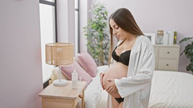 Sıcak bir yatak odası ortamında karnına hafifçe dokunan İspanyol bir kadın bekliyor. Annelik ve sükuneti somutlaştırıyor..