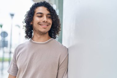 Genç Latin adam gülümsüyor. Kendine güveniyor. Caddenin kenarına bakıyor.