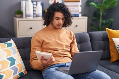 Genç Latin adam evde dizüstü bilgisayar okuyor.