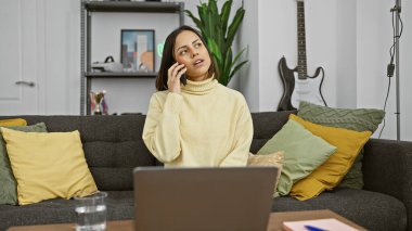 Sarı kazaklı İspanyol kadın modern bir oturma odasında telefonla konuşuyor. Kanepe ve gitarla..