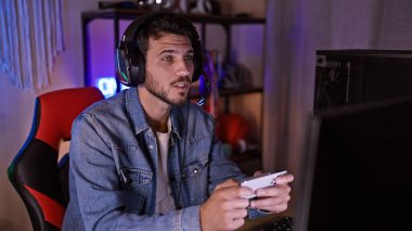 Karanlık bir odada oynayan, kulaklık takan ve elinde bir kumanda tutan İspanyol bir adam.