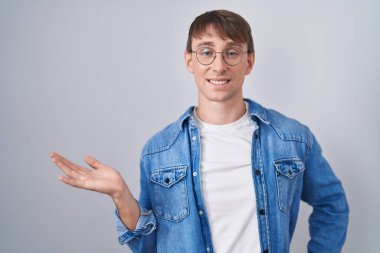 Beyaz, sarışın, gözlüklü, neşeli gülümseyen, elinde avucuyla kameraya bakan bir adam.. 