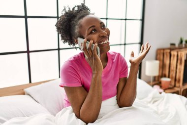 Afrika kökenli Amerikalı bir kadın akıllı telefondan konuşuyor. Yatak odasında oturuyor.